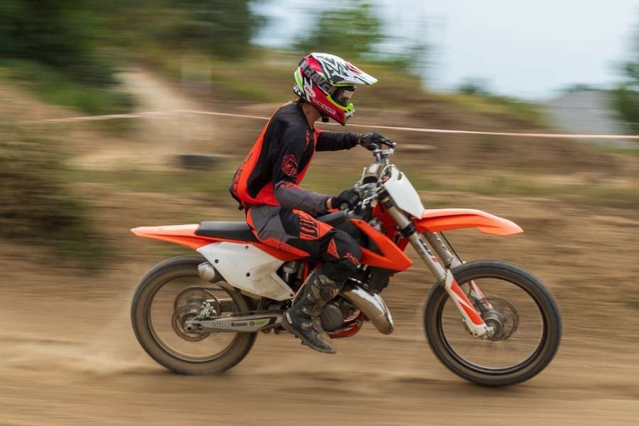 Un pilote en tenue rouge et noire lancé à pleine vitesse sur une moto orange lors d'une compétition moto de motocross sur piste en terre.