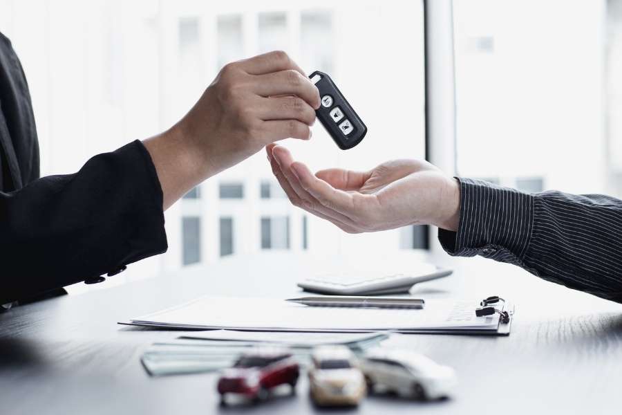 Un vendeur remet les clés d'un véhicule à un client lors de la signature d'un contrat de location de voiture longue durée.